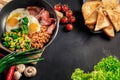 Healthy breakfast with fried eggs, bacon, beans, toasts, mushrooms, broccoli and fresh salad on black background