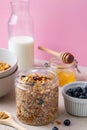 Homemade granola with raisin, seeds, peanut and hazelnut in glass jar, milk bottle, honey and blueberries on pink background. Royalty Free Stock Photo