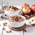 Healthy breakfast. Oatmeal with nuts and apples on white wooden background.