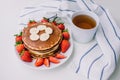 Healthy breakfast. Pancakes with strawberries, bananas, cup of black tea on white background with white towel