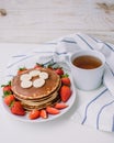 Healthy breakfast. Pancakes with strawberries, bananas, cup of black tea on white background with white towel