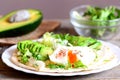 Healthy breakfast with a poached egg, avocado slices, chinese cabbage, lettuce, tortilla, sauce and spices