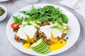 Healthy breakfast. Poached eggs on toast with avocado pieces, arugula, mizuna and chard leaves and cherry tomatoes on a plate on a Royalty Free Stock Photo