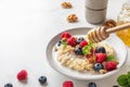 Healthy breakfast. Poring honey in a plate with quinoa porridge with fresh berries, nuts and mint on white background