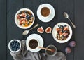 Healthy breakfast set. Bowls of oat granola with yogurt, fresh blueberries and figs, coffee, honey, over black wooden