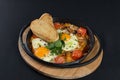 Healthy breakfast shakshuka - fried eggs, onion, bell pepper, tomatoes and spices in cast iron stewpan on old wooden plank Royalty Free Stock Photo