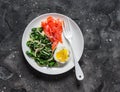 Healthy breakfast, snack - boiled egg, braised spinach, smoked salmon on a dark background, top view Royalty Free Stock Photo