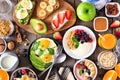 Healthy breakfast table scene with fruit, yogurts, smoothie bowl, oatmeal, nutritious toasts and egg skillet, above view over wood