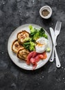 Healthy brunch - poached egg, smoked salmon, romaine salad and savory pancakes on a dark background, top view