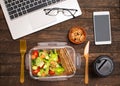 Healthy business lunch at workplace. Salad, salmon, avocado and nuts lunch box on working desk with laptop, smartphone, glasses Royalty Free Stock Photo