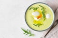 Healthy cauliflower soup with poached egg, olive oil and arugula in a ceramic bowl. Light grey concrete background.
