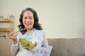 Healthy Asian 60s aged woman enjoys eating tasty Buddha salad mix bowl in her living room Royalty Free Stock Photo