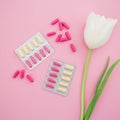 Healthy composition with vitamins pill and white flowers on pink background. Flat lay, top view.