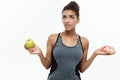 Healthy and diet concept - beautiful sporty African American make a decision between donut and green apple. Isolated on Royalty Free Stock Photo