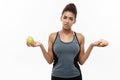 Healthy and diet concept - Beautiful sporty African American make a decision between donut and green apple. Isolated on Royalty Free Stock Photo