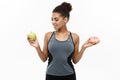 Healthy and diet concept - Beautiful sporty African American make a decision between donut and green apple. Isolated on Royalty Free Stock Photo