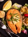 Grilled salmon fish steak with fresh vegetables salad, lemon and grill zucchini on black plate. Healthy and diet food Royalty Free Stock Photo