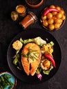 Grilled salmon steak and vegetables on the grill on black background. Vertical top view, close-up. Red fish with garlic Royalty Free Stock Photo