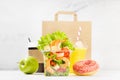 Healthy daily diet plan - set of orange juice, tropical salad with shrimps in plastic box, pink donut, packet in white interior. Royalty Free Stock Photo