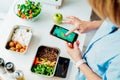 Healthy diet plan for weight loss, daily ready meal menu. Woman using meal tracker app on phone while weighing lunch box Royalty Free Stock Photo