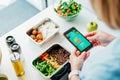 Healthy diet plan for weight loss, daily ready meal menu. Woman using meal tracker app on phone while weighing lunch box Royalty Free Stock Photo