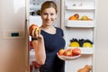 Healthy Eating Concept. Happy woman with apple standing at the opened fridge with fruits, vegetables and healthy food Royalty Free Stock Photo