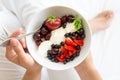 Healthy eating concept. Women`s hands holding bowl with cottage cheese with cream, strawberry, cherry, gooseberry and blueberry