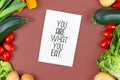 Healthy eating concept with `You are what you eat` text card on brown background with salad, zucchini, tomatoes, potatoes and bell Royalty Free Stock Photo