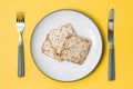 Healthy eating. Crispbread made from oats, wheat, flax and sesame seeds on a plate and cutlery on a yellow background. Top view