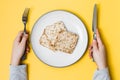 Healthy eating. Crispbread made from oats, wheat, flax and sesame seeds on a plate and hands hold cutlery on a yellow background.