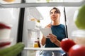 Woman making list of necessary food at home fridge