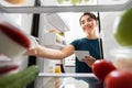 Woman making list of necessary food at home fridge