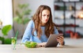 Healthy eating. happy young girl eating salad with tablet pc in morning in kitchen Royalty Free Stock Photo