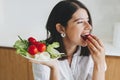 Healthy eating. Young happy woman eating cherry tomato and holding plate with lettuce, tomatoes