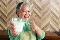 Healthy elderly Asian woman holding a glass of skim milk, showing thumbs up.