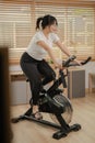 A healthy, fit Asian woman in sportswear is doing cardio at home, exercising on a fitness bike Royalty Free Stock Photo