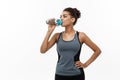Healthy and Fitness concept - beautiful African American girl in sport clothes drinking water after workout. Isolated on