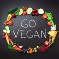 Healthy food background. Circle of fresh vegetables, fruits, nuts, berries with handwritten phrase Go Vegan on black