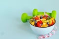 Healthy food. Bowl of vegetarian fresh fruit salad made of different fruits, dumbbells, measuring tape: banana, kiwi, apple, Royalty Free Stock Photo