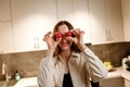 Healthy food concept. Young happy woman holding cherry tomato at eyes and smiling on background of modern white kitchen. Home Royalty Free Stock Photo