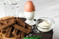 Healthy food. A boiled egg in a white ceramic stand stands on a wooden table next to rye croutons and white sauce