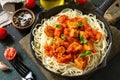 Healthy food, Italian pasta. Spaghetti with chicken and vegetables in tomato sauce in a cast iron skillet on a stone countertop. Royalty Free Stock Photo