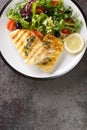 Healthy food serving grilled fish cod with fresh vegetable salad and leaf lettuce mix and lemon close-up in a plate. Vertical top Royalty Free Stock Photo