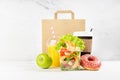 Healthy food set with coffee cup, orange juice, shrimp salad in plastic pack, apple, donut, packet, fruit in white interior. Royalty Free Stock Photo