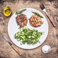 Healthy foods appetizing grilled pork steak with green salad of cucumber, spinach and arugula white plate on wooden rustic ba