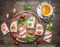 Healthy foods sandwiches with red fish, cherry tomatoes and salami on a cutting board, cup of tea with thyme on wooden rust