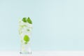 Healthy fresh tonic with green mint, ice cubes, soda, striped straw in misted glass on white wood table, pastel green color.