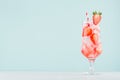 Healthy fresh tonic with strawberry slices, ice cubes, soda, striped straw in misted glass on white wood table, pastel green color