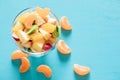 Top view fruit salad in glass bow and tangerine slices on turquoise table.