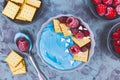 Healthy fruit smoothie bowl dyed with natural blue spirulina powder and topped with red raspberry and cranbery and biscuits Royalty Free Stock Photo